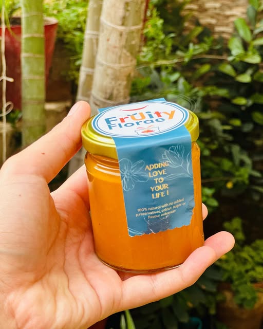 A hand holding a Fruity Florae branded jar against a garden backdrop