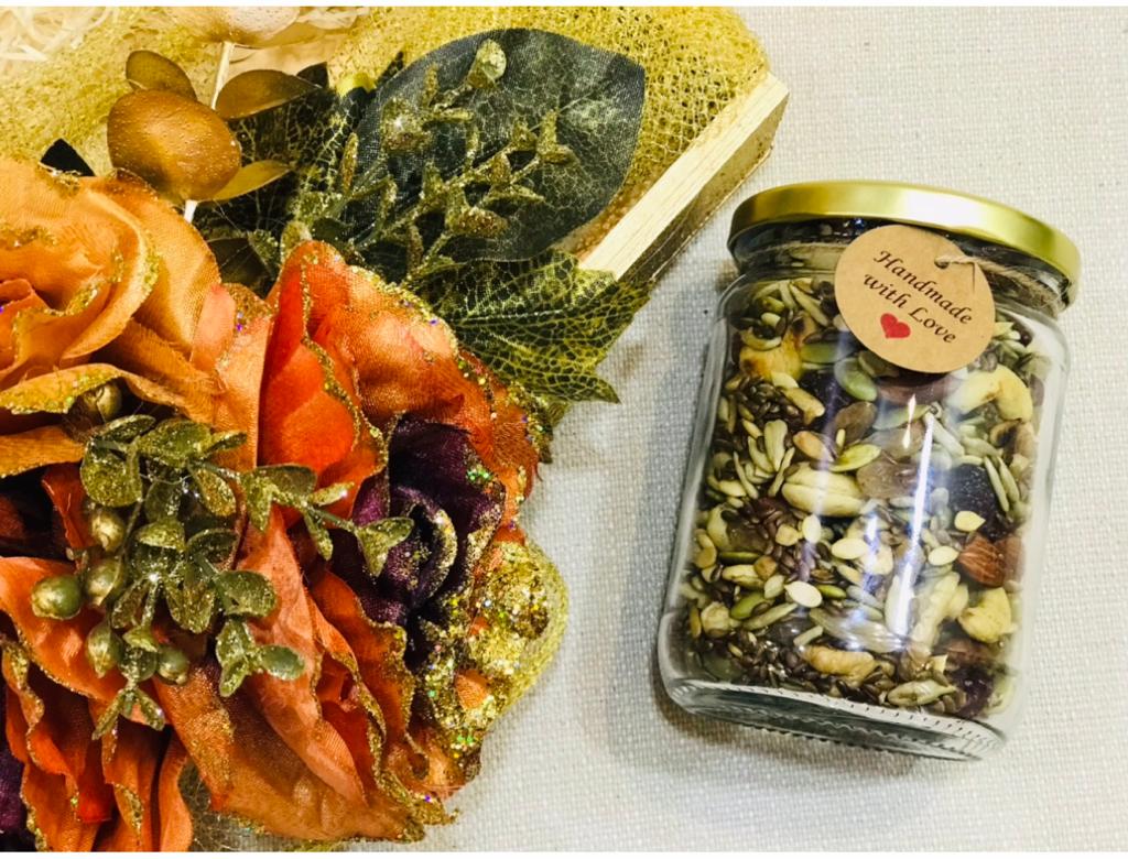 A jar of mixed seeds and dry fruits with a handmade-with-love tag beside floral gift packaging